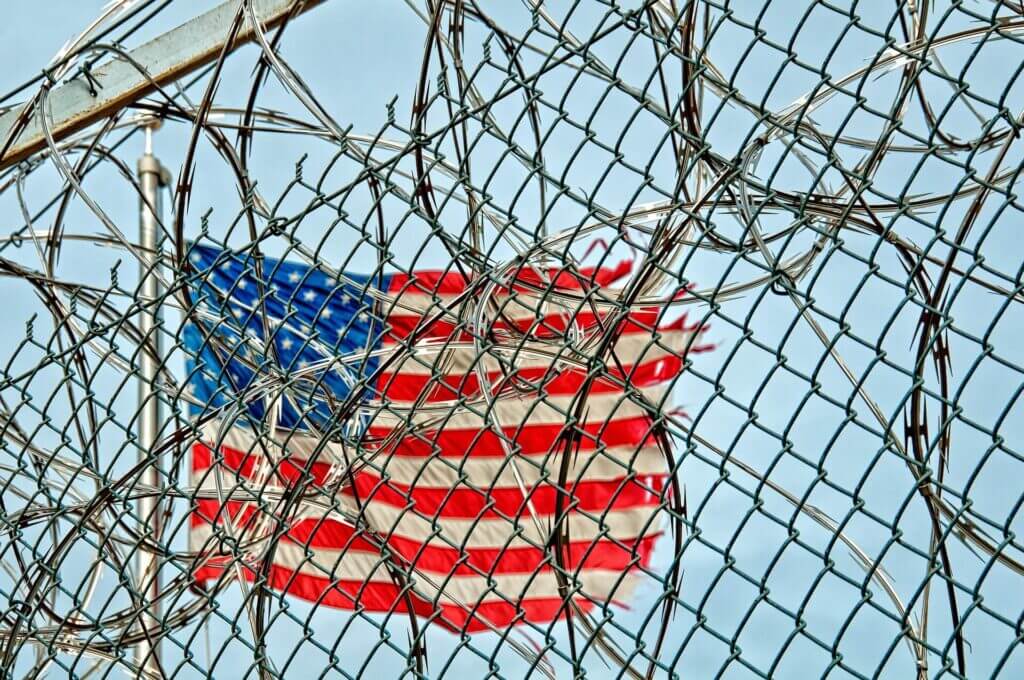 Bandera de Estados Unidos detrás de un alambrado - Este artículo habla acerca del creciente número de niños no acompañados en la frontera y la colaboración de FEMA.